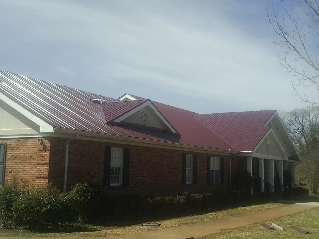 Red metal roof with gabled entries on a long brick building, from a Hail Damage Roof Repair job in Wickliffe