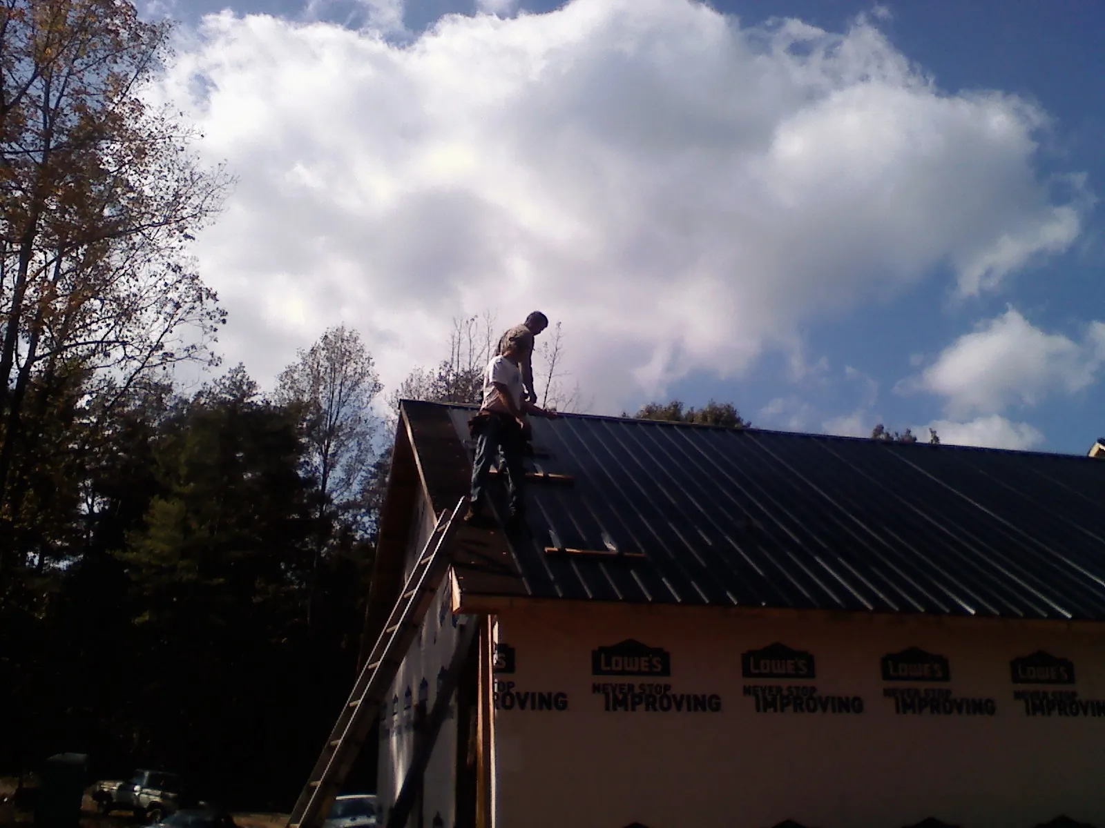 Roofer fastening dark metal panels high against a cloudy sky, from a Roof Inspection job in Wickliffe